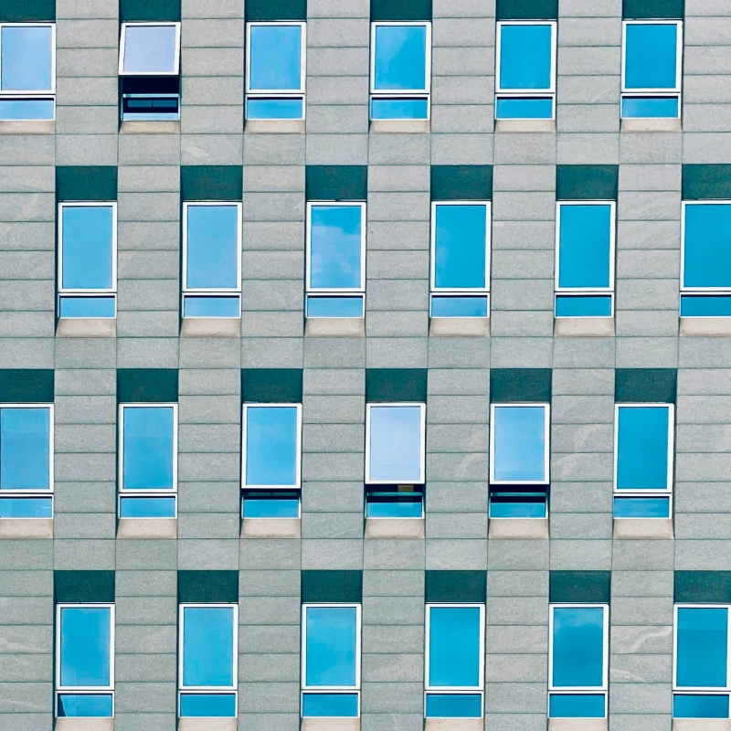 Fassade eines modernen Gebäudes mit regelmäßig angeordneten rechteckigen Fenstern und blauer Spiegelverglasung.