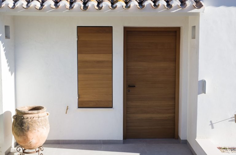 Eingangsbereich eines mediterranen Hauses mit Holztür, passendem Fensterladen und heller Putzfassade.