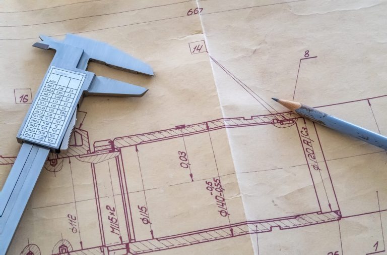 Technische Zeichnung mit Maßangaben, darauf liegen ein Messschieber und ein gespitzter Bleistift.